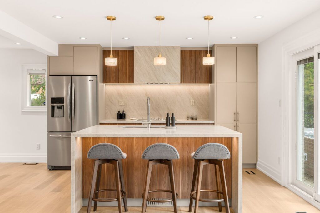 Renovated kitchen with walnut and taupe flat-panel cabinetry and a waterfall stone island